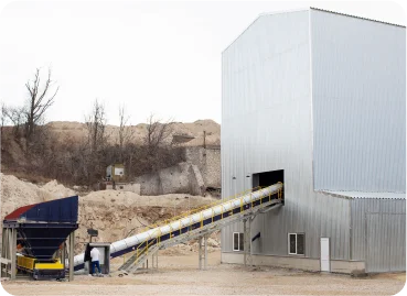 Industrial processing facility with conveyor belt system and dump trucks.