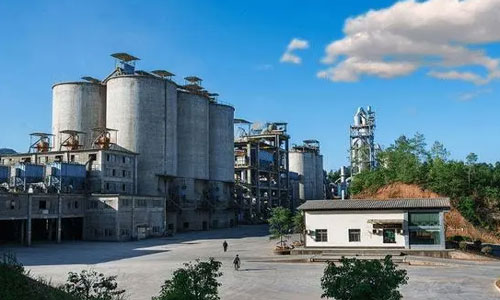 Cement plant with concrete silos and processing towers under blue sky.
