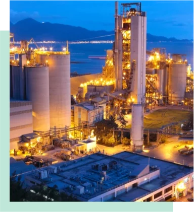 Illuminated cement plant at night with tall towers and silos.
